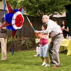 man with little girl outside hitting a large red, white, and blue pinata