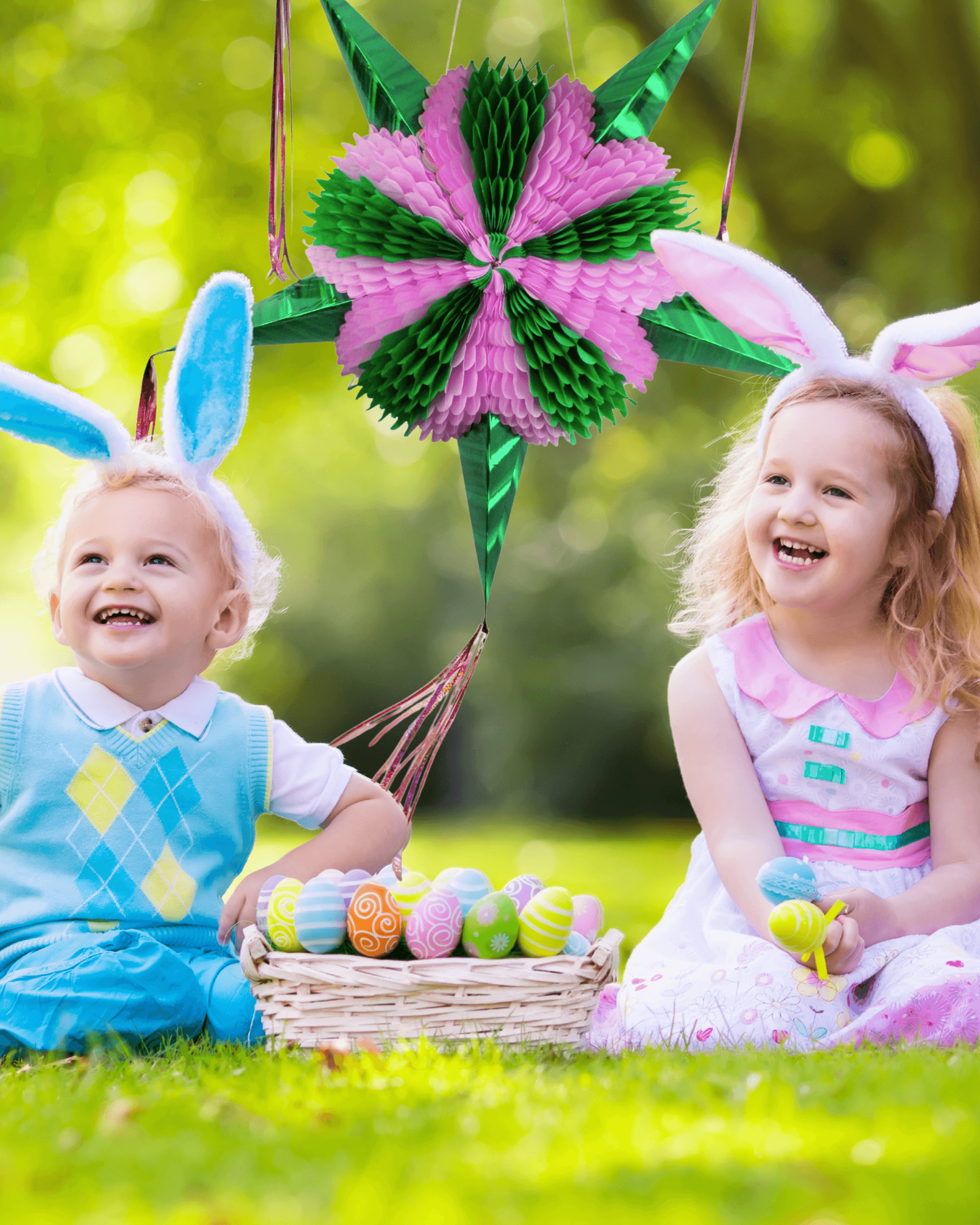 Two children wearing bunny ears sitting on grass with Easter eggs and a decorative pinata.